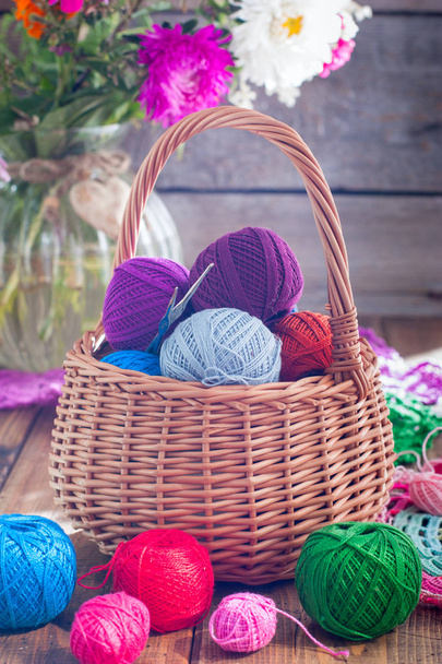 Multi-colored balls of cotton thread for crocheting in a wicker basket on a wooden table, selective focus - Φωτογραφία, εικόνα