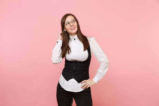 Young pensive successful business woman in glasses keeping hand near head looking aside isolated on pastel pink background. Lady boss. Achievement career wealth concept. Copy space for advertisement - Photo, Image