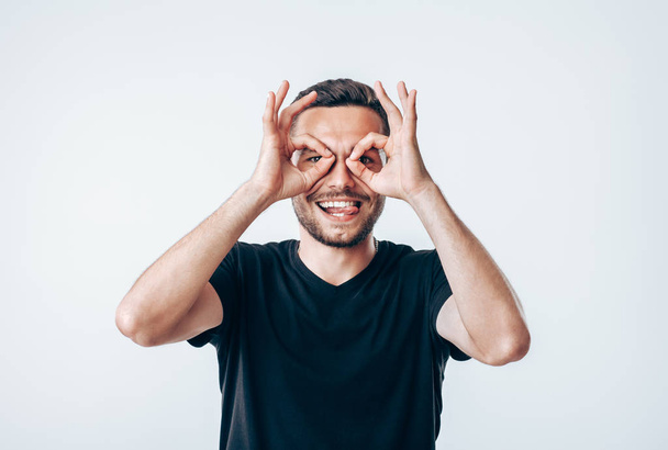 Young creative man holding fingers near eyes like glasses. Fun concept - Fotó, kép