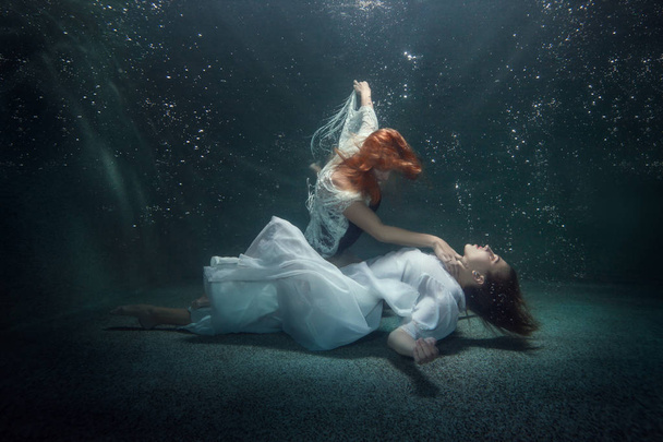 Fiatal nő hazudik-ra-a alja víz alatt, egy másik nő tartja a kezét a nyakát. - Fotó, kép