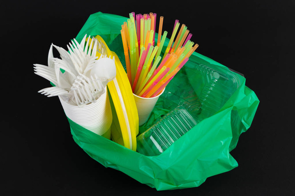 Plastic waste danger ecology concept with full garbage bag and colorful single use straws cutlery cups plates casserole boxes isolated on black background - Photo, Image
