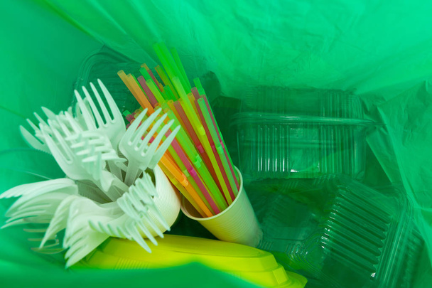 Inside of green plastic bag with single use cutlery plates straws cup and package boxes as ecology environment waste pollution concept - Photo, Image