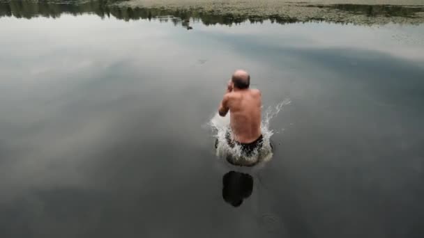 Kaukasische volwassen man springen uit houten pier in lake. - Video