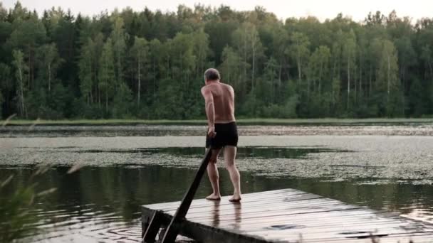 Kaukaski dojrzały mężczyzna, skacząc z pomostem nad jeziorem. - Materiał filmowy, wideo