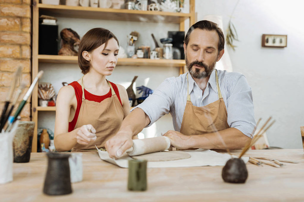 Bearded dark-haired handicraftsman giving master class for woman - Photo, Image