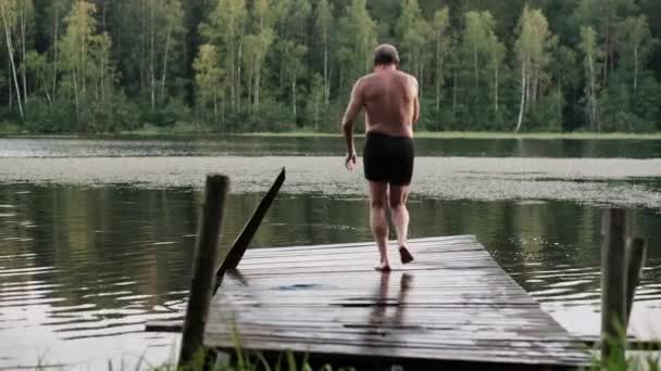 Kaukasische volwassen man springen uit houten pier in lake. - Video