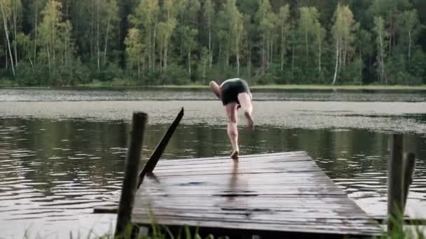 Взрослый кавказский мужчина прыгает с деревянного пирса в озеро
. - Кадры, видео