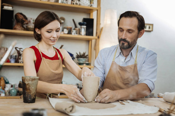Bearded man wearing striped shirt looking at female potter - Zdjęcie, obraz