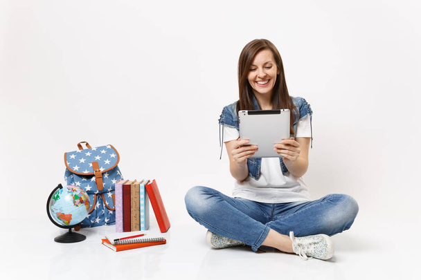 Nuori nauraa nainen opiskelija tilalla tabletin tietokoneen avulla, videopuhelu, istuu lähellä maailmaa, reppu, koulukirjat eristetty valkoisella taustalla. Koulutus lukion yliopisto college
 - Valokuva, kuva