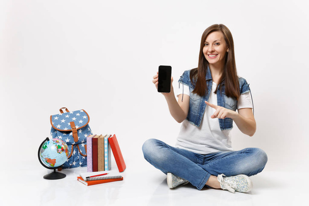 Jovem estudante apontando dedo indicador no celular com tela vazia preta em branco perto do globo, mochila, livros escolares isolados em fundo branco. Educação no ensino médio faculdade universitária
 - Foto, Imagem