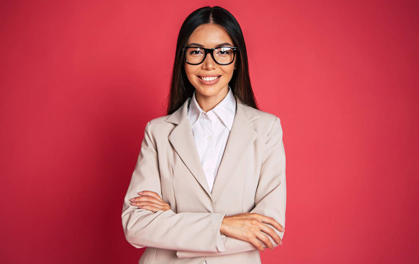 Portrait of young businesswoman fixing glasses on red background - Photo, Image