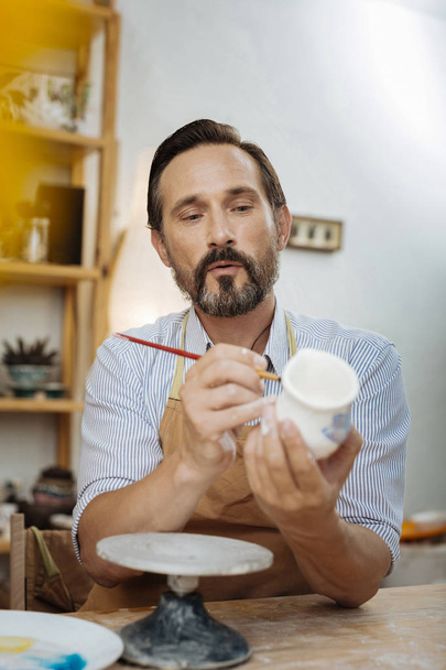 Dark-eyed bearded ceramist wearing apron and working - Фото, изображение