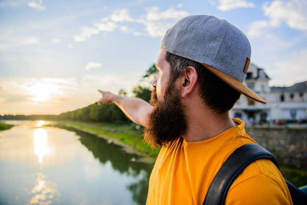 Guy in front of blue sky at evening time admire landscape. Man in cap enjoy sunset while stand on bridge. Take moment to admire sunset nature beauty. River sun reflection. Enjoy pleasant moment - Fotó, kép