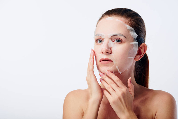 Beautiful young caucasian woman applying paper sheet mask on her face isolated on white background. Beauty skin care concept. Cosmetology. - Φωτογραφία, εικόνα