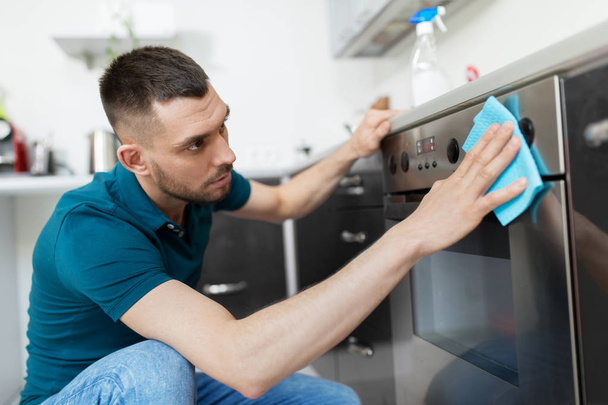 man with rag cleaning oven door at home kitchen - Foto, Imagen
