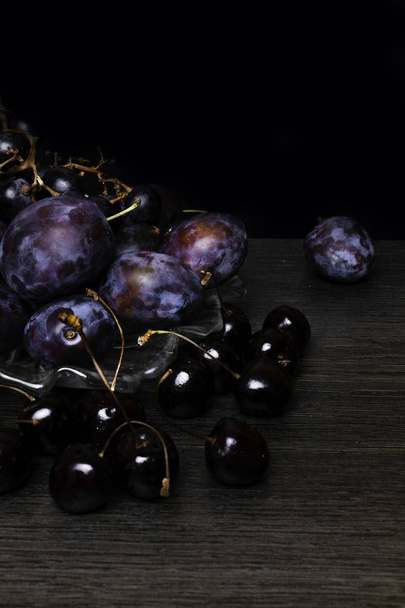 nature morte avec prune, raisin, cerise sur table en bois, fond noir. Une saine alimentation. Alimentation végétalienne
 - Photo, image