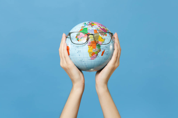 Close up female hold in hands geographic political world globe with glasses isolated on blue background. Learning about countries. Education in high school university concept. Travel journey abroad - Photo, Image