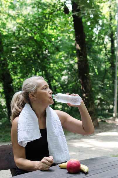Seniorin trinkt Wasser und schleicht in der Natur. Raum für Text. - Foto, Bild