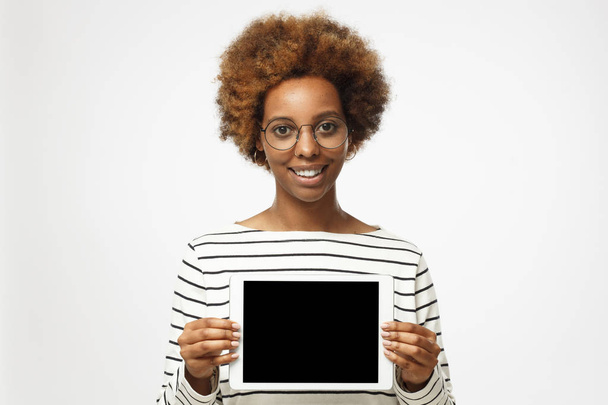 Studio picture of smiling African American woman isolated on gray background standing and holding tablet, showing blank black screen with happy smile - Foto, immagini