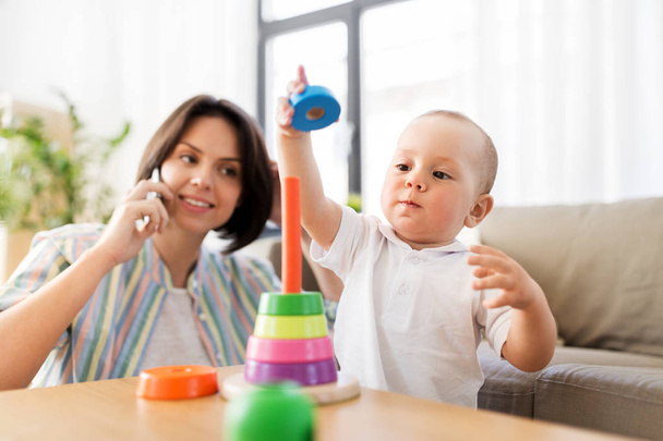 baby boy playing toy and mother calling on phone - Фото, изображение