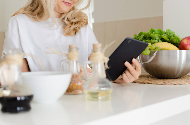Immagine ritagliata di donna adulta che utilizza tablet in cucina alla ricerca di recepis
. - Foto, immagini