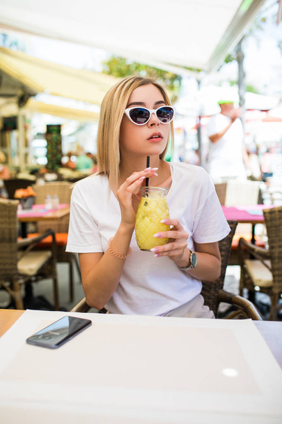 Joven hermosa mujer en gafas de sol redondas con cóctel en la terraza de la cafetería
 - Foto, Imagen