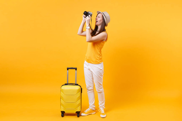 Turisti nainen kesällä rento vaatteita matkalaukku, retro vintage valokuva kamera eristetty keltainen oranssi tausta. Matkustaja matkustaa ulkomaille viikonloppuisin lomalle. Ilmalennon käsite
 - Valokuva, kuva
