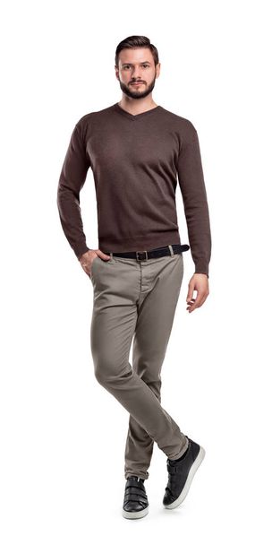 A man in pants and a sweater stands with one leg crossing another on a white background. - Foto, afbeelding