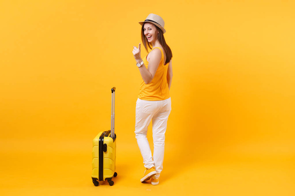 Touristin in sommerlicher Freizeitkleidung, Hut mit Koffer auf gelb-orangefarbenem Hintergrund. Passagierin, die ins Ausland reist, um am Wochenende zu reisen. Flugreise-Konzept - Foto, Bild