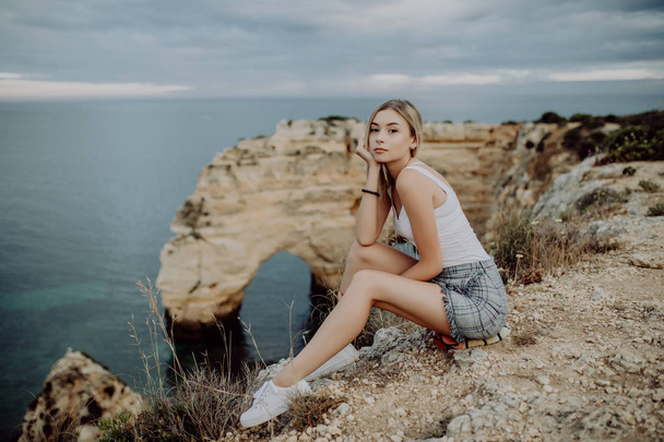 Young blonde Woman sitting on the rocks top by the ocean. - Fotoğraf, Görsel