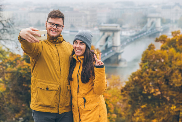 couple taking selfie old chain bridge cross danube river on background. budapest, hungary. autumn is coming - Photo, Image