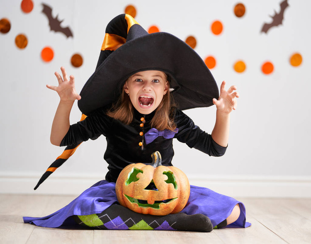 Happy Halloween! Cute little laughing girl in witch costume with a pumpkin. - Фото, зображення