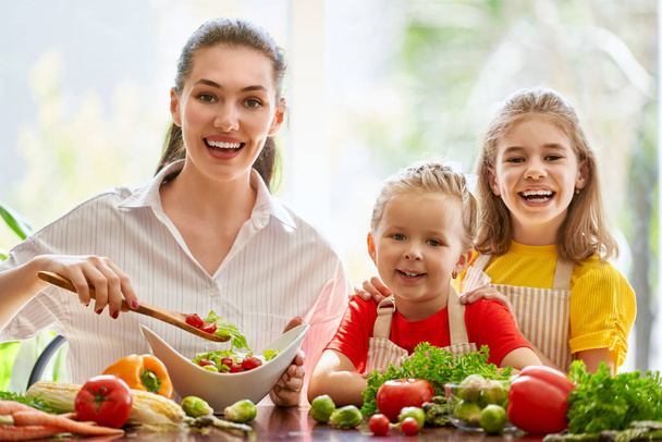 Healthy food at home. Happy family in the kitchen. Mother and children daughters are preparing the vegetables. - Foto, afbeelding