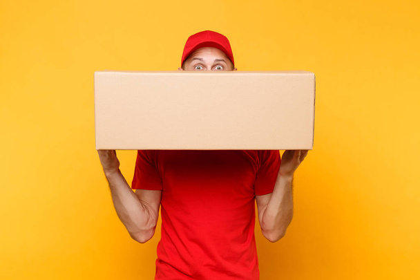 Delivery man in red uniform isolated on yellow orange background. Professional male employee courier or dealer in cap t-shirt holding empty cardboard box. Receiving package service concept. - Photo, Image