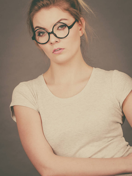 Bored focused or grumpy blonde teenage woman wearing nerdy eyeglasses, white t shirt. Teenager fashion concept. - Fotoğraf, Görsel