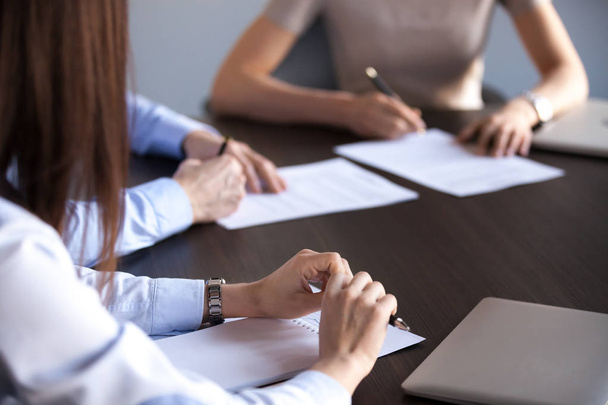 Close up of business partners signing contracts during company briefing or team meeting, people sitting at shared table at conference, putting signature on documents or agreements at negotiations - Foto, Imagem