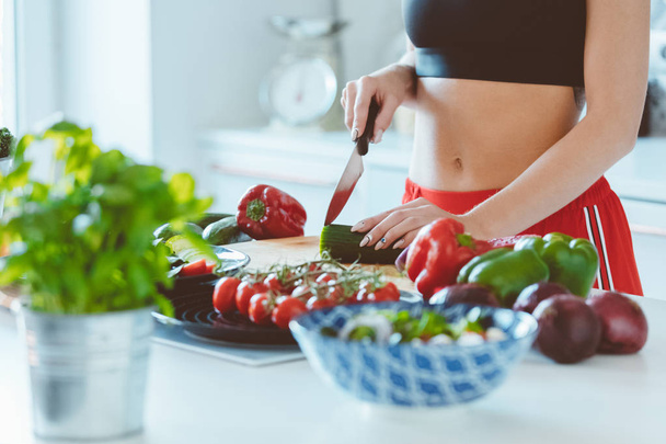 Young woman wearing sport clothes standing in the kitchen at home and making vegetable salad. Close up of hands, unrecognizable person.  - Foto, Bild