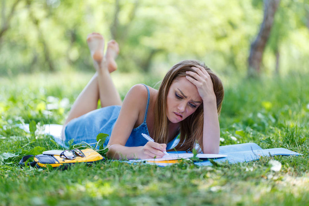 Beautiful young woman writing in her notebook, in the park - Photo, image
