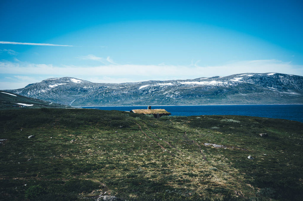 Jotunheimen εθνικό πάρκο τοπίο στο Oppland της Νορβηγίας. Παλιά παραδοσιακή νορβηγική καλύβες στην ακτή της μια ορεινή λίμνη και ένα βουνό στο παρασκήνιο. - Φωτογραφία, εικόνα