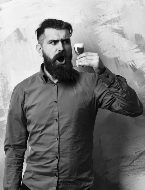 Bearded man, long beard. Brutal caucasian surprised hipster with moustache in brown shirt holding alcoholic red shot on colorful texture background. - Foto, Bild