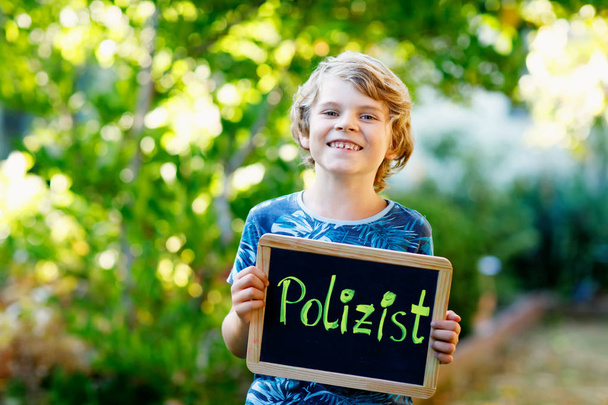 Happy little kid boy with chalk desk in hands. Healthy adorable child outdoors On desk - police officer - in German as dream profession of beautiful schoolkid - Fotó, kép