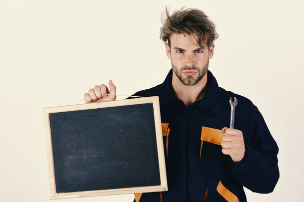 Service and construction presentation concept. Man with beard and serious face holds chalkboard on white background. Mechanic or repairer holds blackboard with copy space. Plumber with spanner in hand - Foto, Imagen