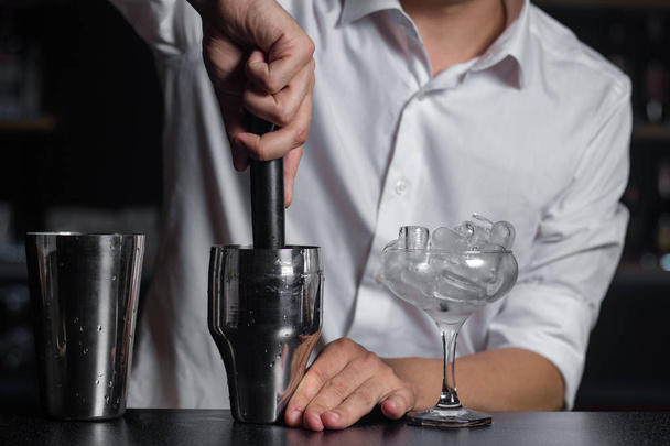Egy üveg chalet tele jéggel és shaker állva a bárban számláló. Csapos összenyomja a friss gyümölcsök által a madler. Folyamat-ból egy koktél elkészítéséhez. - Fotó, kép