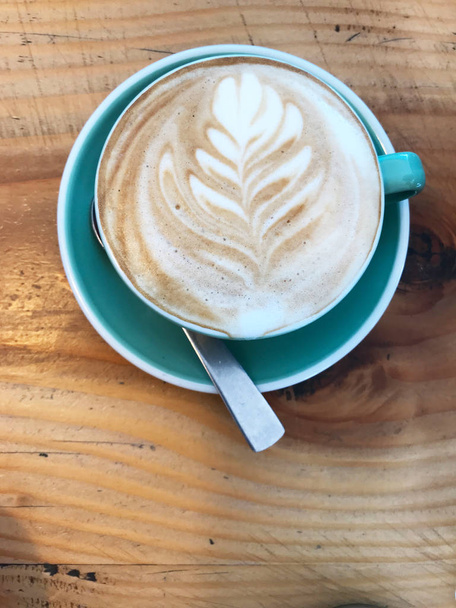 's morgens wakker worden door het drinken van een kopje koffie met melk schuim blad patroon koffie art on rustieke houten tafel - Foto, afbeelding