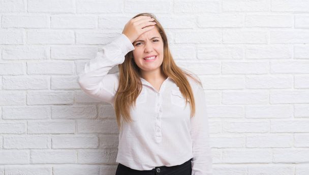Young adult business woman over white brick wall stressed with hand on head, shocked with shame and surprise face, angry and frustrated. Fear and upset for mistake. - Photo, image