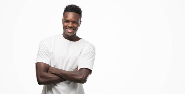 Jonge Afro-Amerikaanse man dragen witte t-shirt blij gezicht lachend met gekruiste armen kijken naar de camera. Positief persoon. - Foto, afbeelding