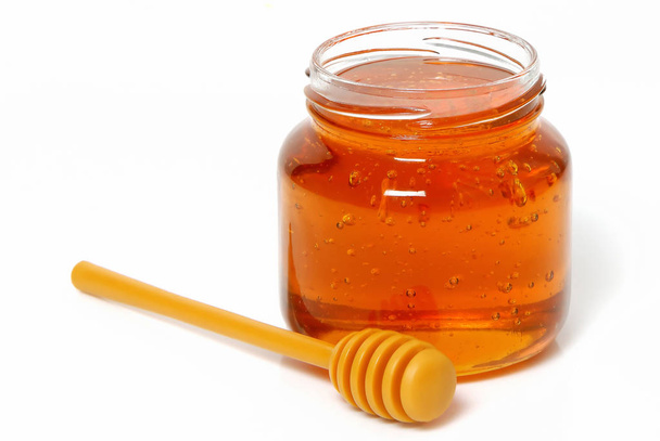 Glass jar with honey and dipper on white background - Fotó, kép