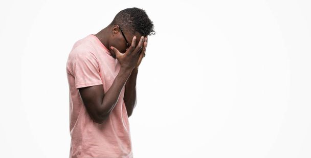 Молодой африканский американец в розовой футболке с грустным лицом, прикрывающим лицо руками во время плача. Концепция депрессии
. - Фото, изображение