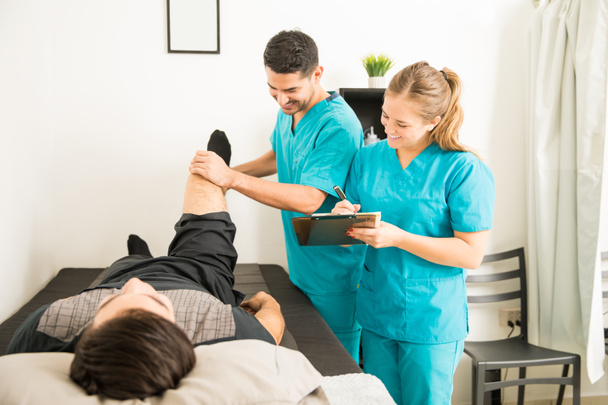 Mladí fyzioterapeutů kontrola pacienta nohy a příprava poznámky v nemocnici - Fotografie, Obrázek