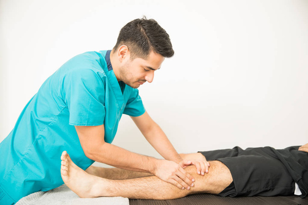 Mann bekommt Kniebehandlung von junger Physiotherapeutin im Krankenhaus - Foto, Bild